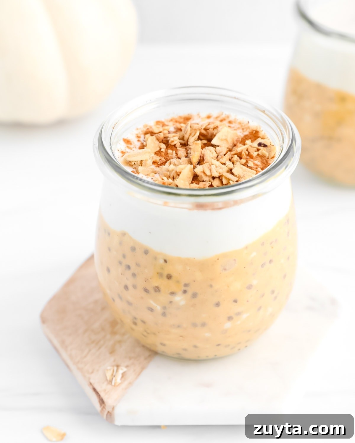 Creamy Pumpkin Pie Overnight Oats Recipe 4 A clear glass filled with overnight oats, vanilla, and granola.