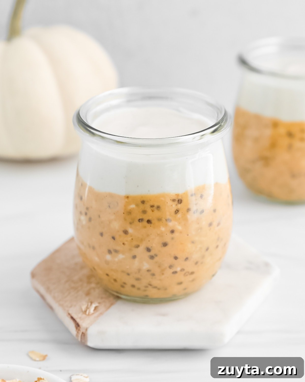 Creamy Pumpkin Pie Overnight Oats Recipe 6 A clear glass filled with pumpkin overnight oats and vanilla yogurt.