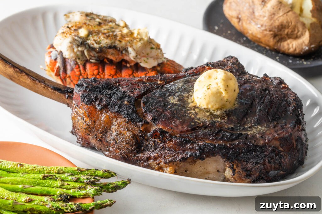 Tomahawk Steak Recipe: Grill and Reverse-Sear 2 cooked tomahawk steak topped with a scoop of compound butter on a plate with a cooked lobster tail. asparagus spears and a baked potato with butter in the background
