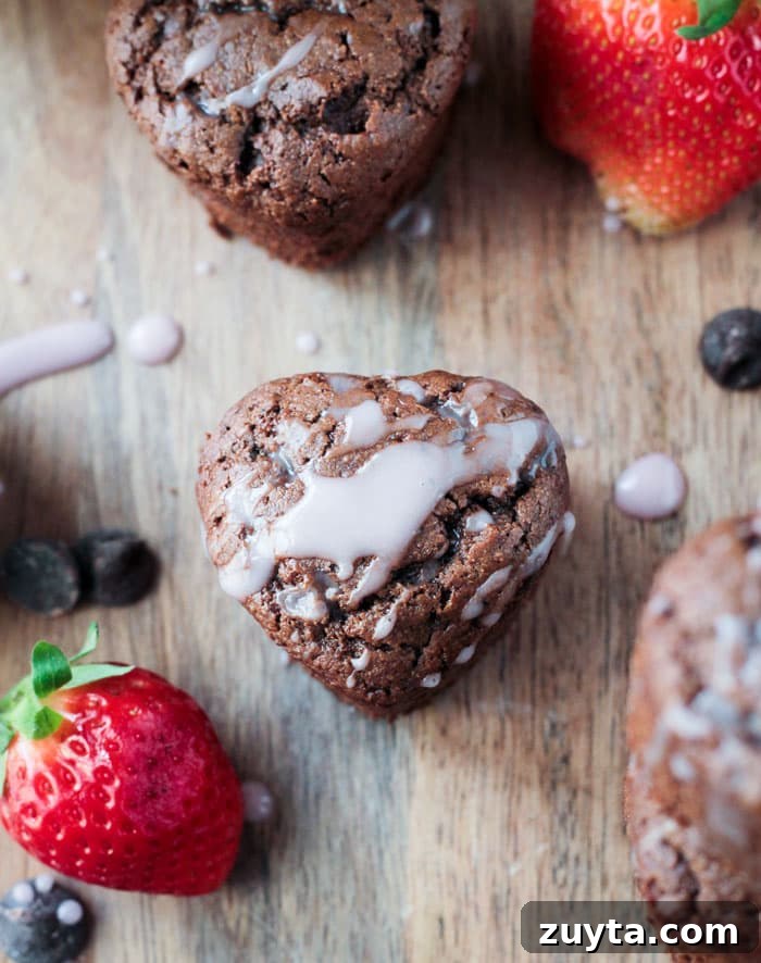 Tahini Chocolate Chip Cupcakes - These adorable little mini cupcakes are perfect for Valentine's Day. Treat your sweetie...or your kids...or yourself...to some chocolate indulgence made healthier with no dairy, no eggs, no oil, and no refined sugar. Overhead view of a Tahini Chocolate Chip Cupcake drizzled in pink icing. Fresh strawberries and chocolate chips nearby.