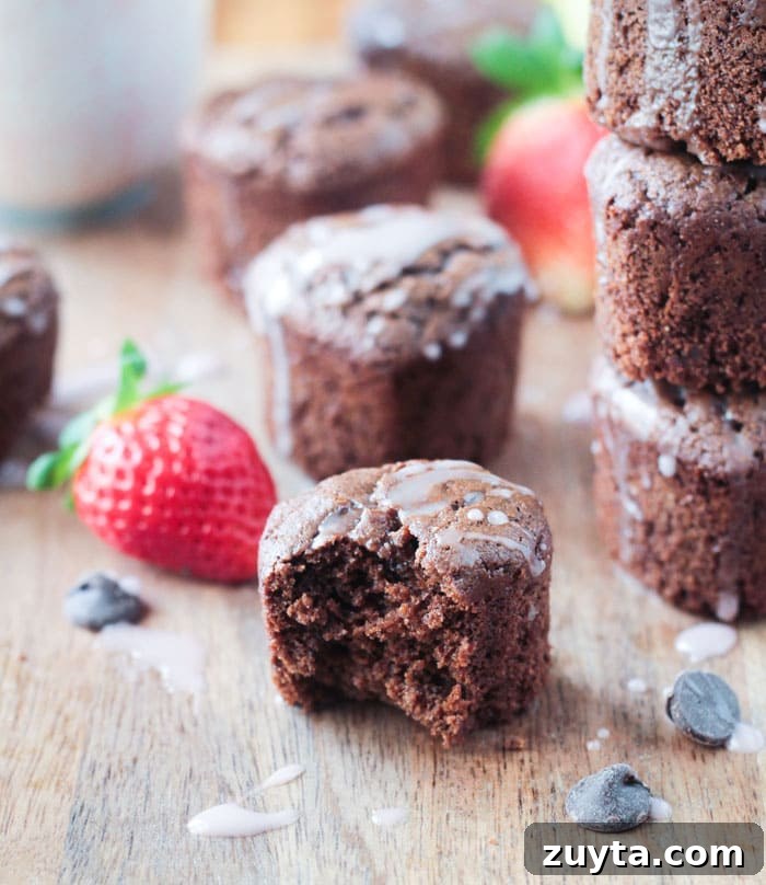 Tahini Chocolate Chip Cupcakes - These adorable little mini cupcakes are perfect for Valentine's Day. Treat your sweetie...or your kids...or yourself...to some chocolate indulgence made healthier with no dairy, no eggs, no oil, and no refined sugar. One Tahini Chocolate Chip Cupcake with a bite taken out. Stack of cupcakes behind and chocolate chips scattered about.