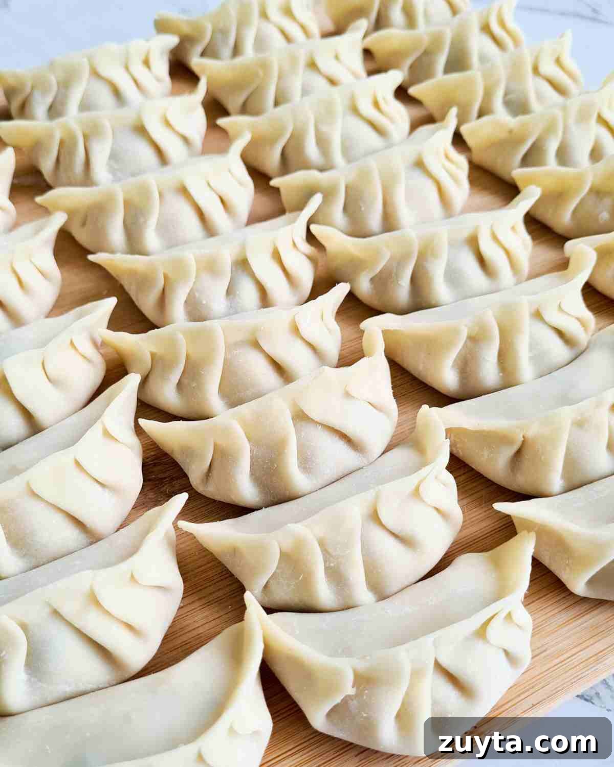 How to Make Authentic Chinese Chicken Dumplings 11 Rows of neatly wrapped dumplings on a wooden chopping board