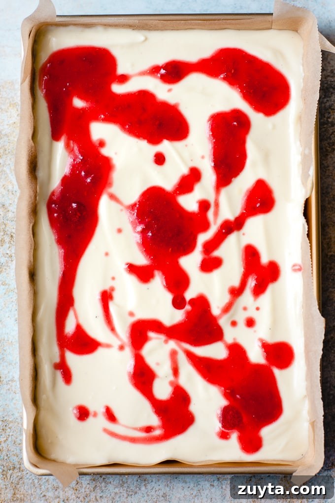 Creamy White Chocolate Raspberry Cheesecake Bars Recipe 6 Raspberry sauce being swirled in to cheesecake.