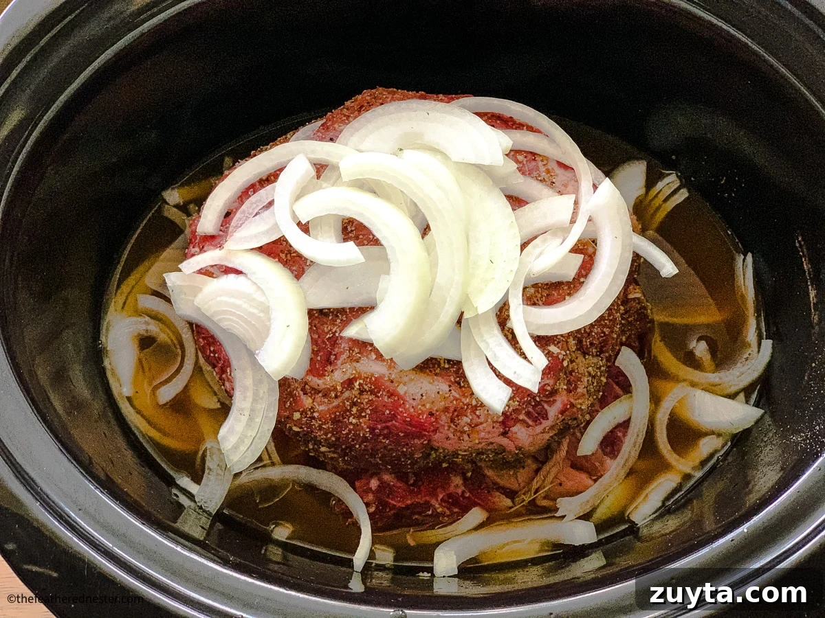 Tender Slow Cooker Shredded Chuck Roast Recipe 7 Seasoned beef with a crock pot and seasoning in the background.