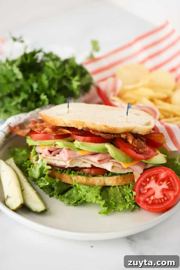 How to Make a Classic Turkey Club Sandwich 2 A white dinner plate with a turkey club sandwich and a side of pickles.