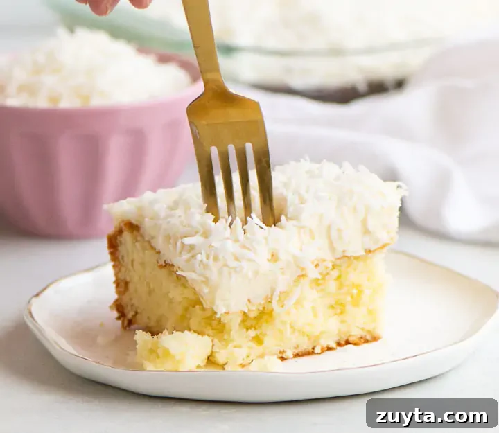Moist Coconut Sour Cream Cake Recipe 2 fork digging into a slice of coconut sour cream cake on a plate