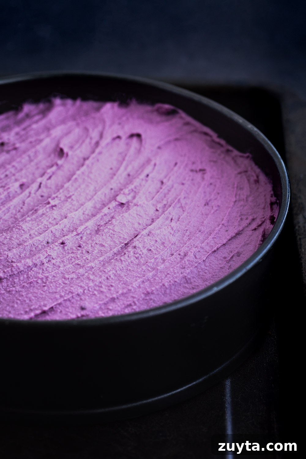 Side angle shot of the purple sweet potato cheesecake batter spread out on the spring foam pan.